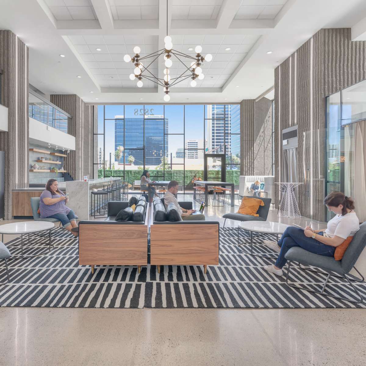 A modern lobby area with seating, a large chandelier, and natural light coming through large windows.