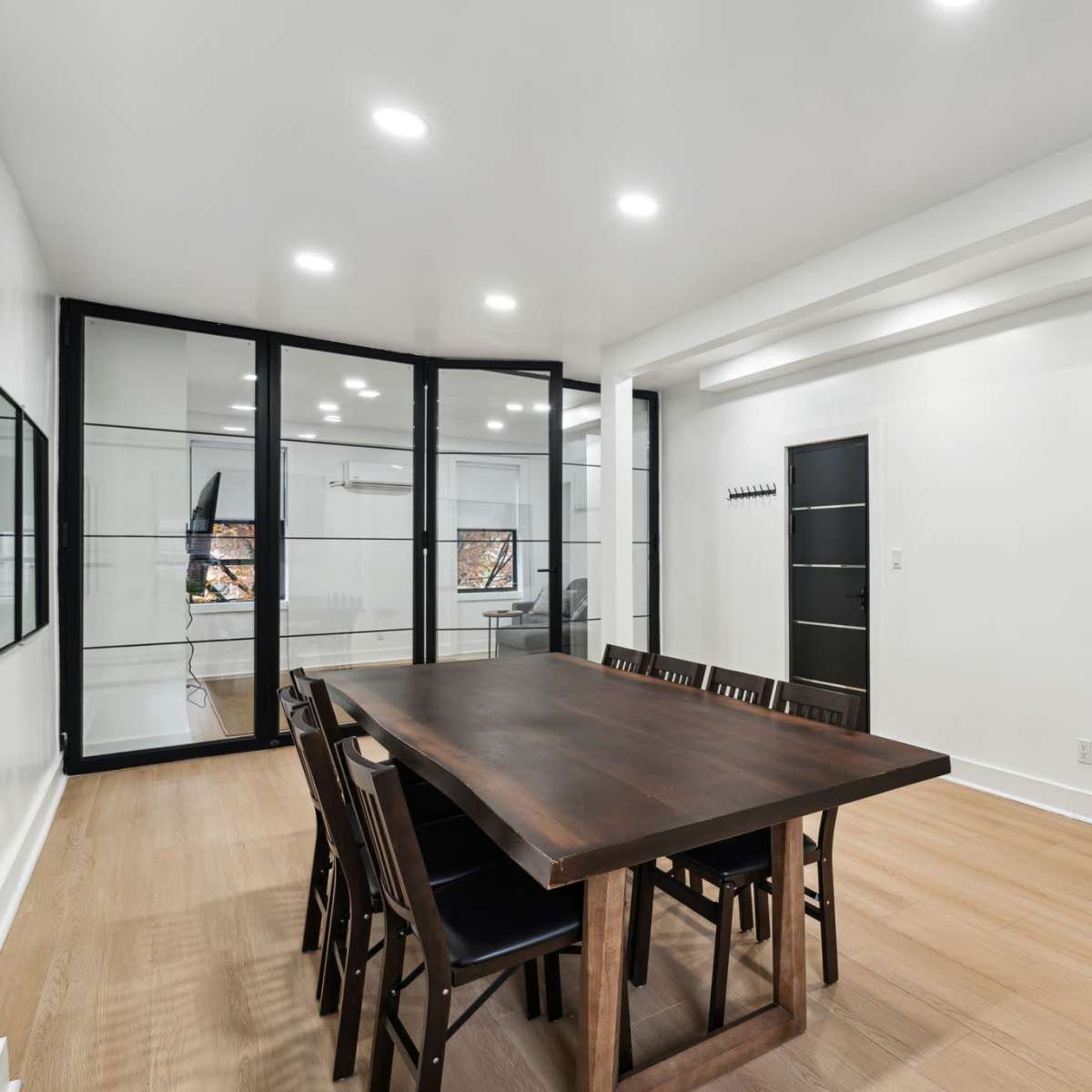 A modern meeting room features a large wooden table surrounded by chairs, with glass partitions and an air conditioning unit on the wall.