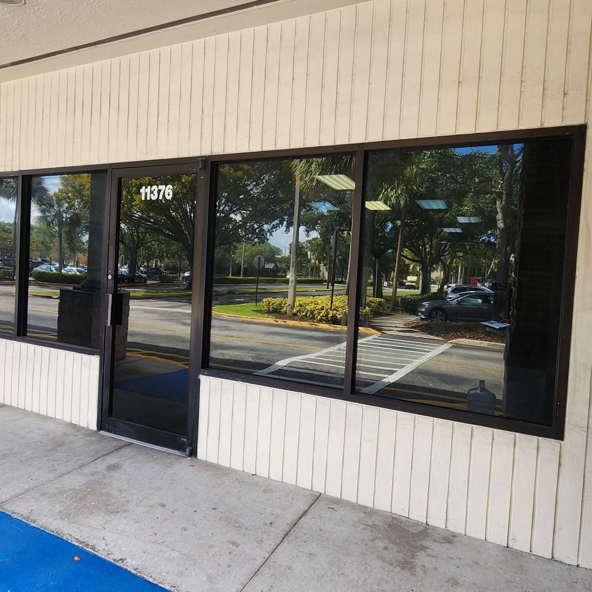 The exterior of a commercial building featuring large glass windows, a black door, and a section of stone siding next to a sidewalk.