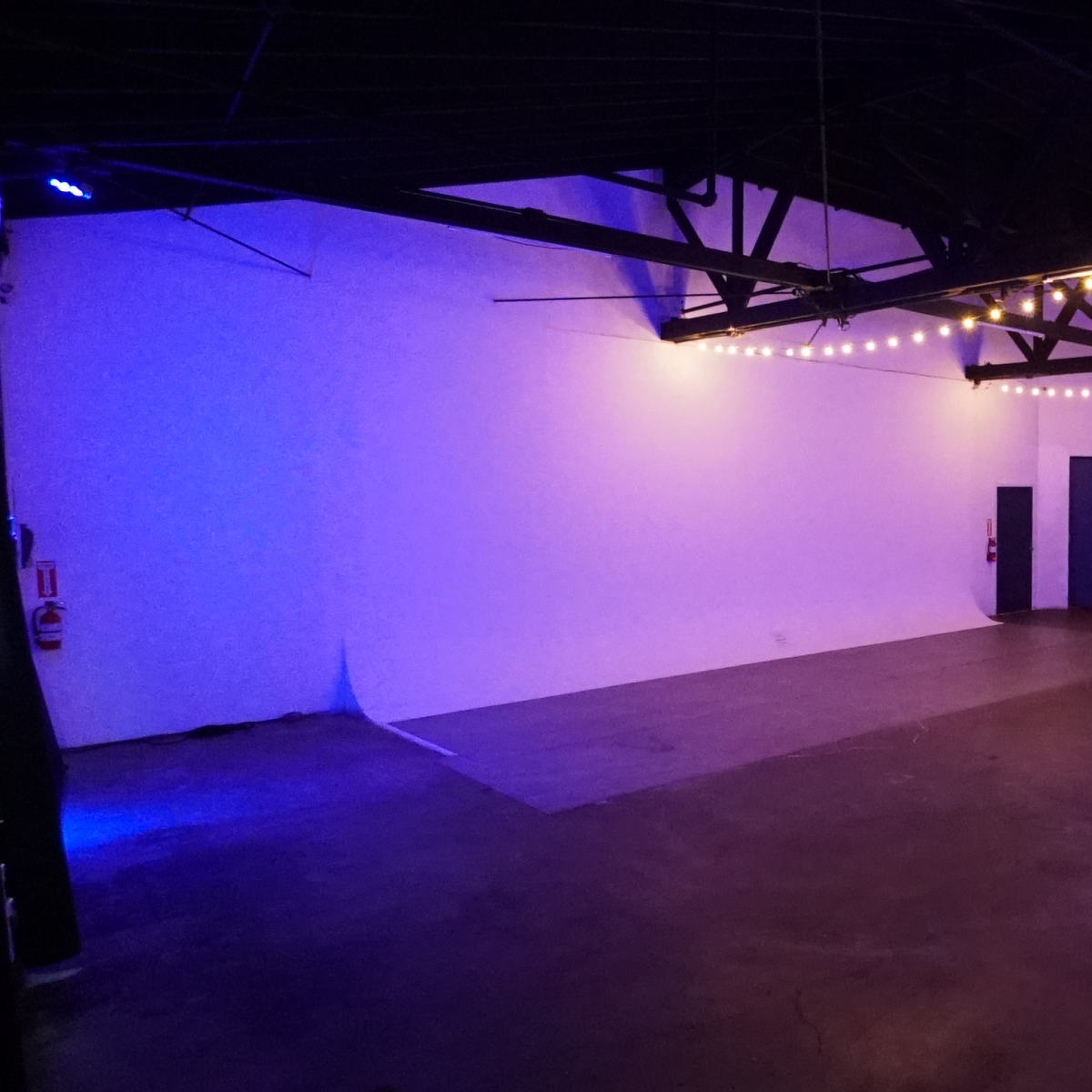 A spacious industrial room with a polished concrete floor, white walls, and purple LED lighting along the ceiling and perimeter.