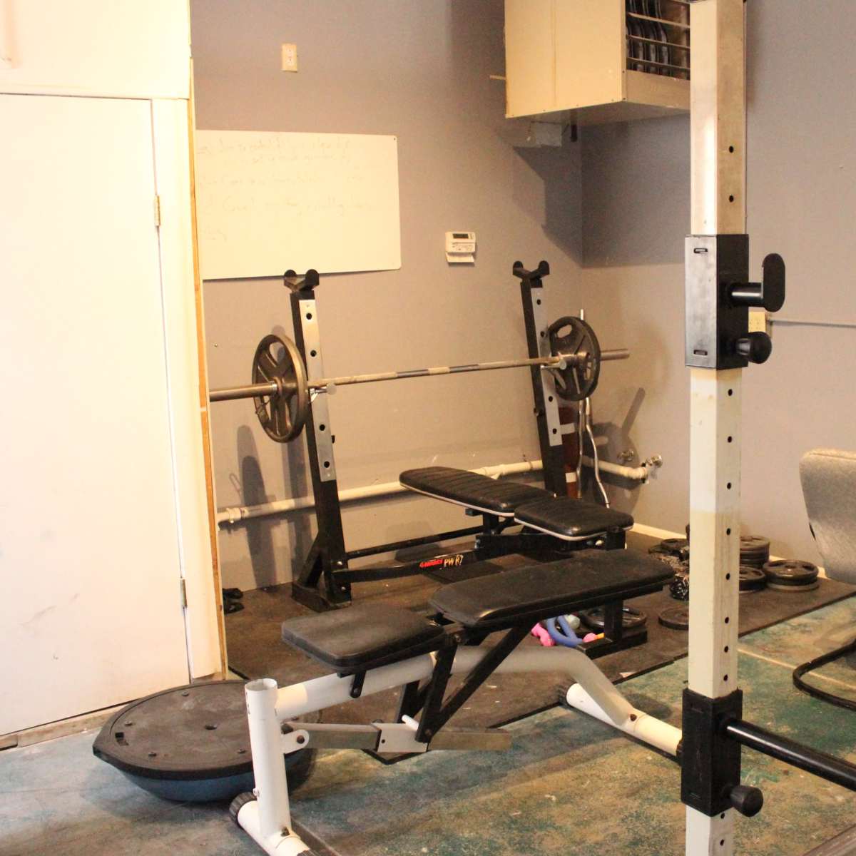 A small gym area with a weight bench, barbell rack, and a chair against a wall.