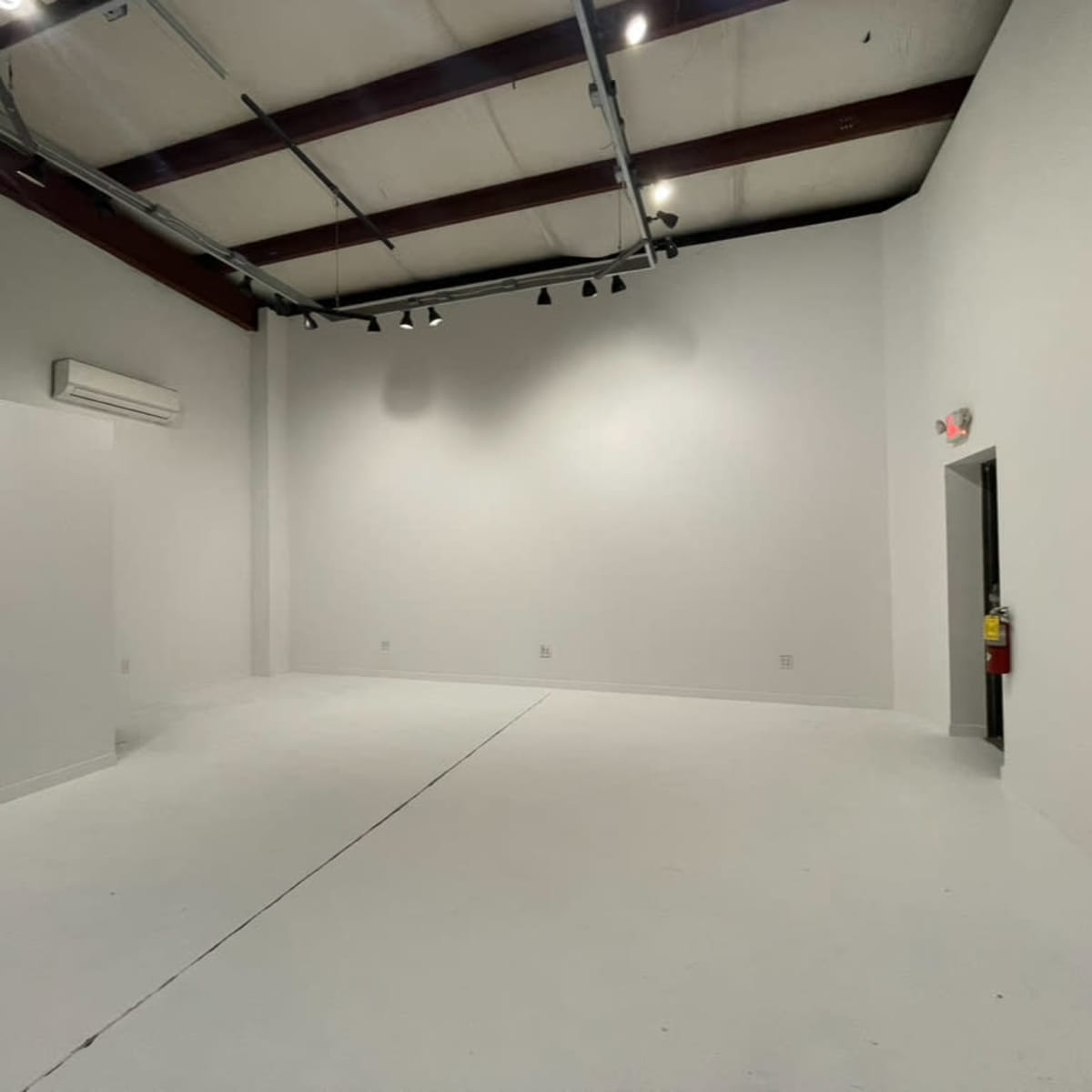 An empty, well-lit room with white walls, a white floor, and a partially open door.