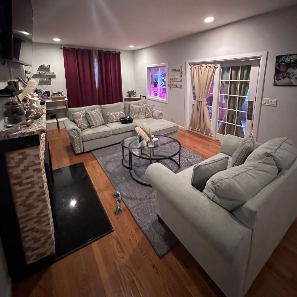 A cozy living room with a pair of light-colored sofas, a glass coffee table, and a fireplace, featuring dark curtains and a door leading to an outdoor area.