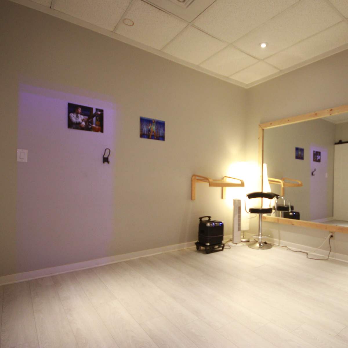 A minimalistic room with a large mirror, a chair, and faint lighting, featuring light-colored walls and wooden accents.