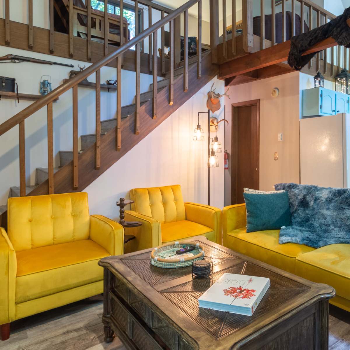 A living room with yellow furniture, a wooden coffee table, and a staircase leading to a loft area.