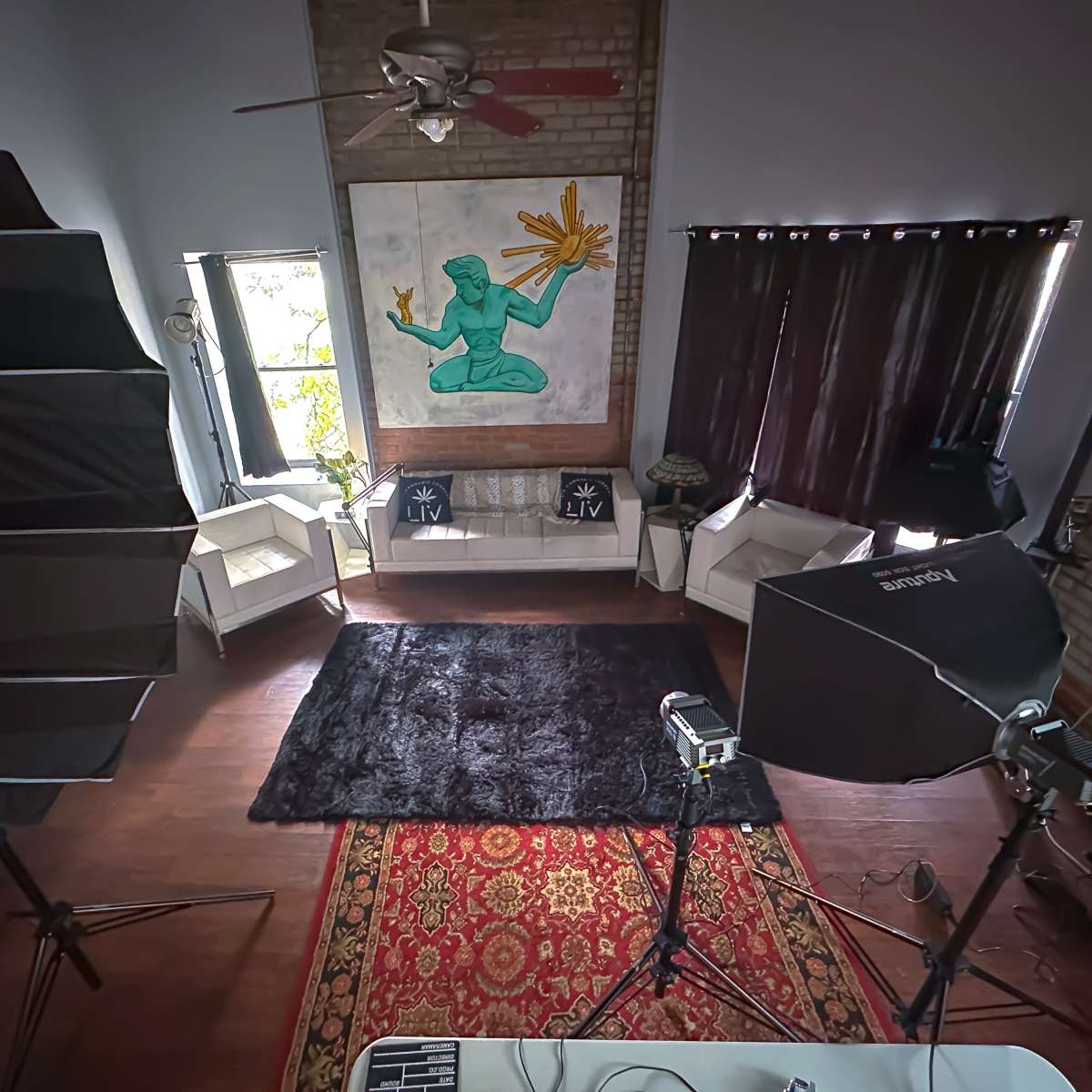 A spacious room features a large mural, two white sofas, and professional photography equipment set up on a patterned rug.