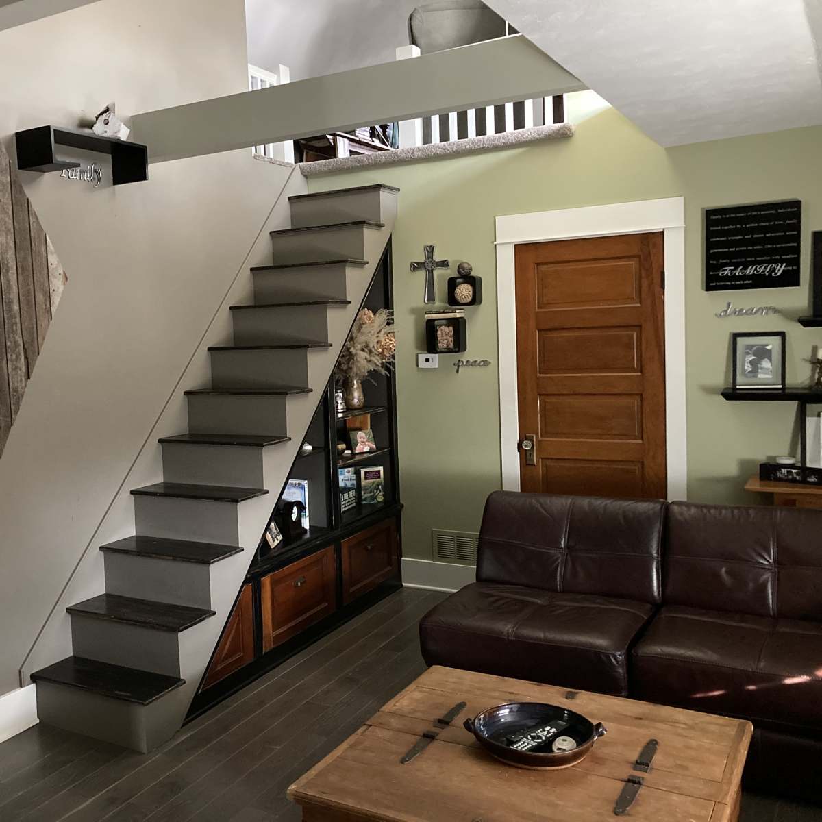 A modern living room with a staircase made of metal steps leading to an upper level, alongside a wooden wall decoration and a brown leather sofa.