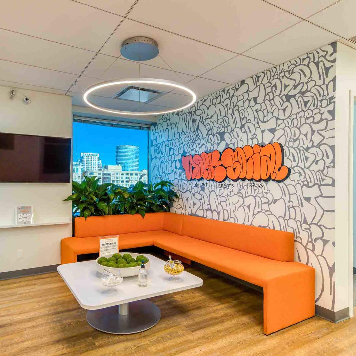 A modern office lounge area with a curved orange sofa, a white coffee table, and a large decorative wall featuring graffiti-style text.