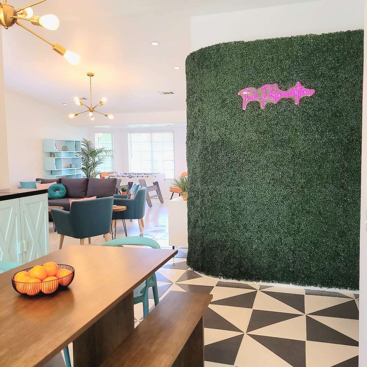 A vibrant interior space featuring a green wall with neon signage, a dining table with a fruit bowl, and modern furniture arranged in a living area.