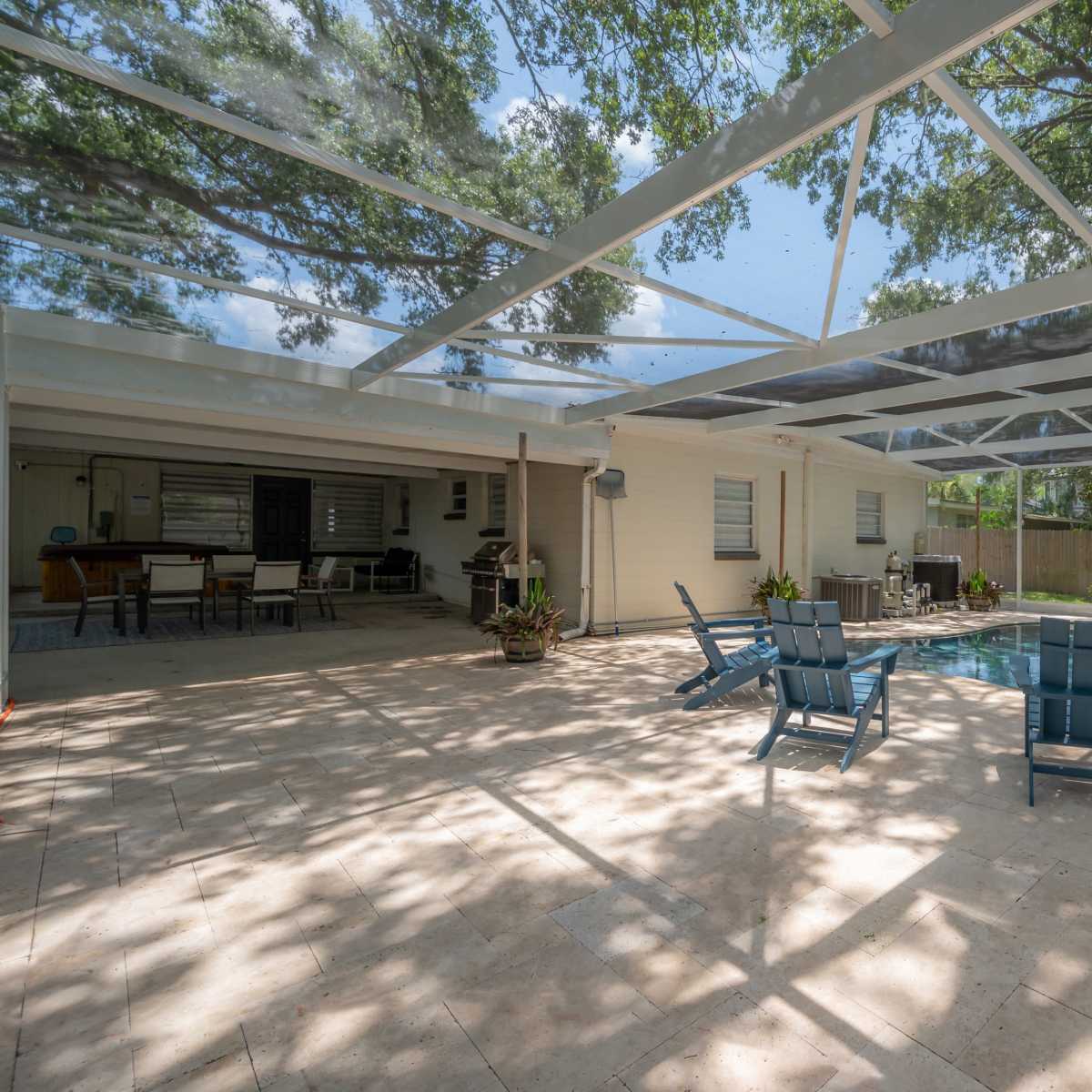 A pool area with tiled flooring, surrounded by a screened enclosure, and featuring lounge chairs and a table in a backyard setting.