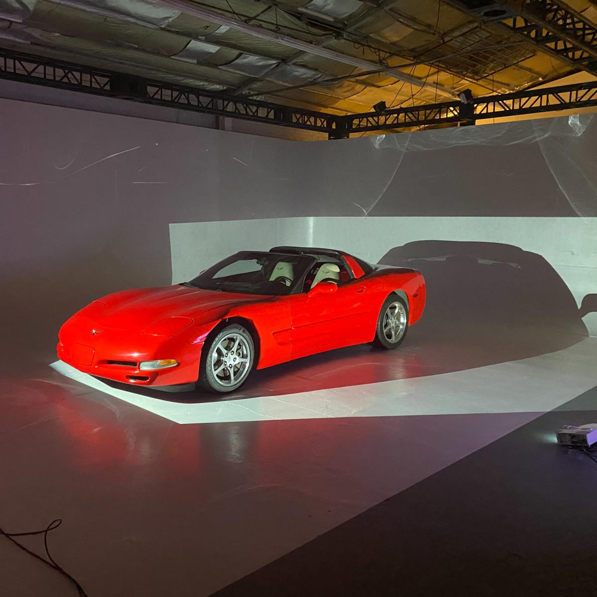 A red sports car is positioned on a white stage with projected lighting creating shadows on the background.