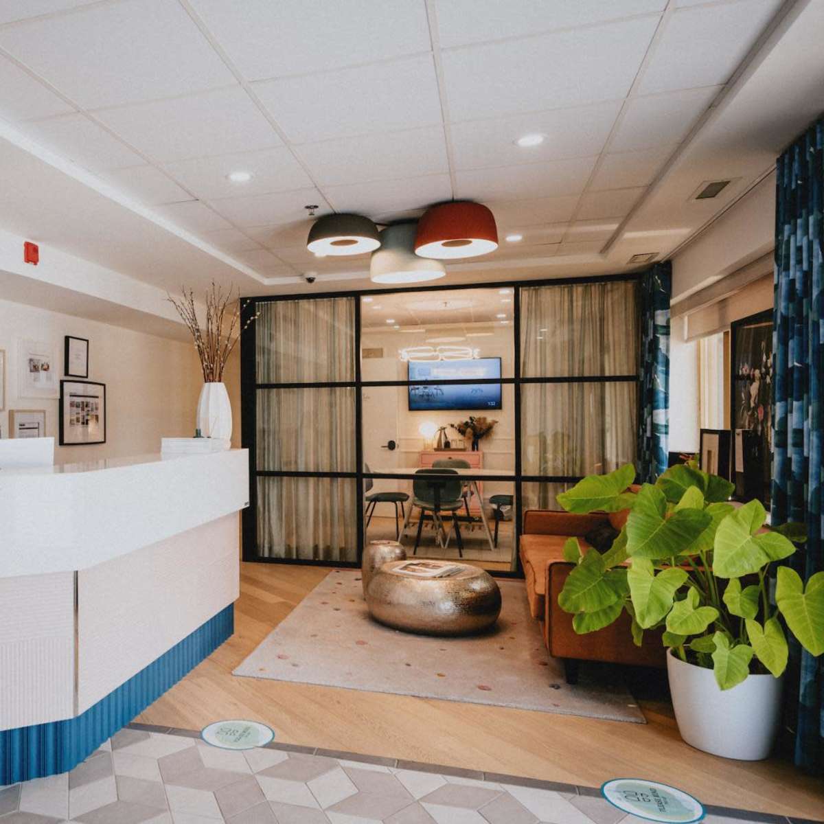 A reception area features a front desk, seating space with a sofa, and a large plant, along with display screens and decorative lighting.
