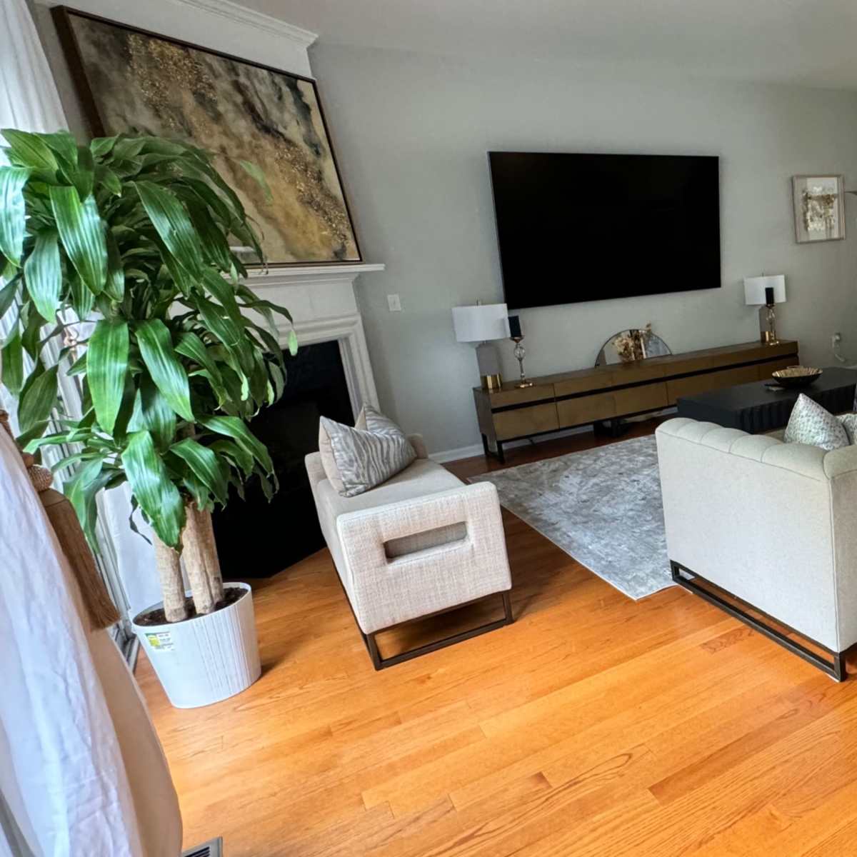 The living room features a large gray sofa, two armchairs, a wall-mounted television, and a dining area visible in the background.
