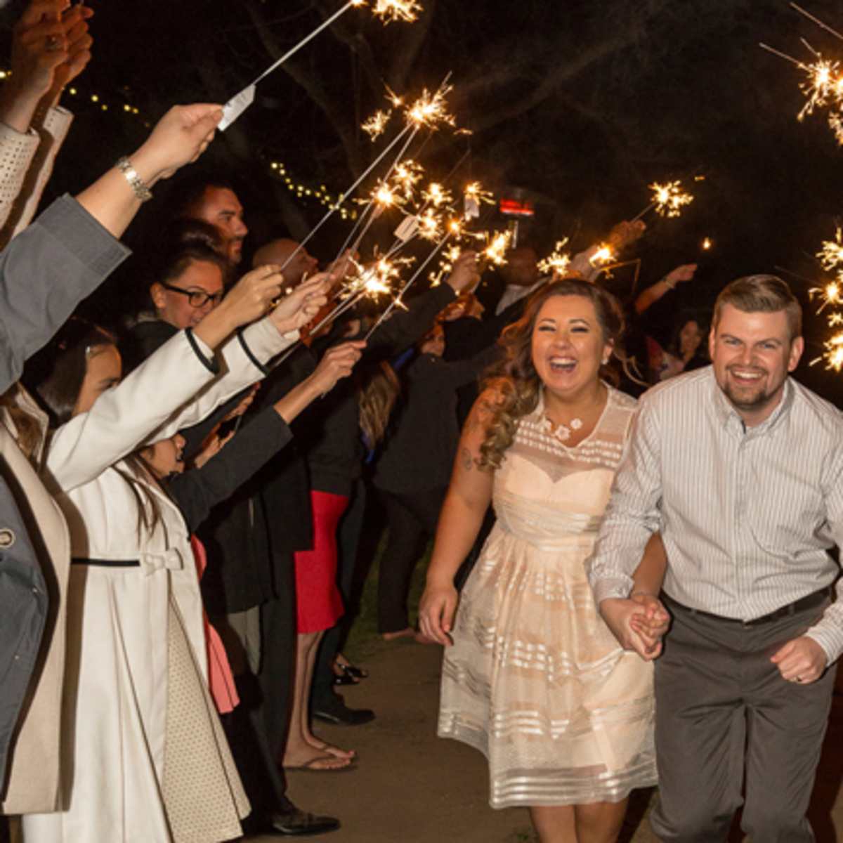 A couple runs through a tunnel of guests holding sparklers in a nighttime celebration.