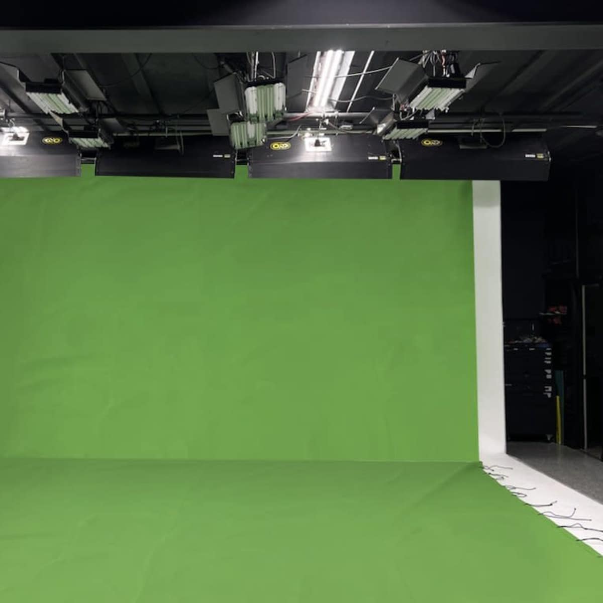 A studio setup featuring a green screen backdrop with overhead lighting equipment.