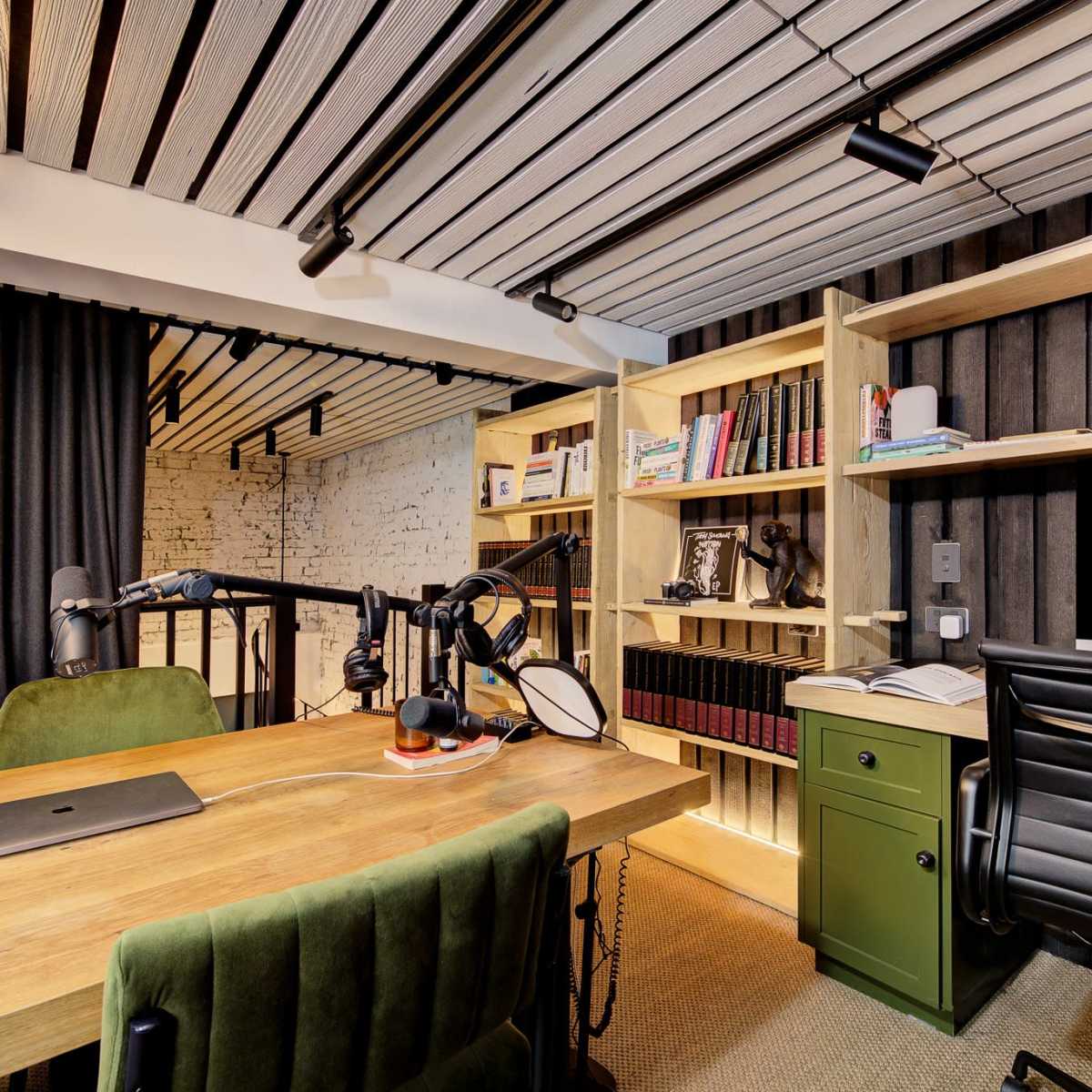 A modern office space featuring a wooden desk with a computer, green chair, shelves filled with books, and a black curtain.