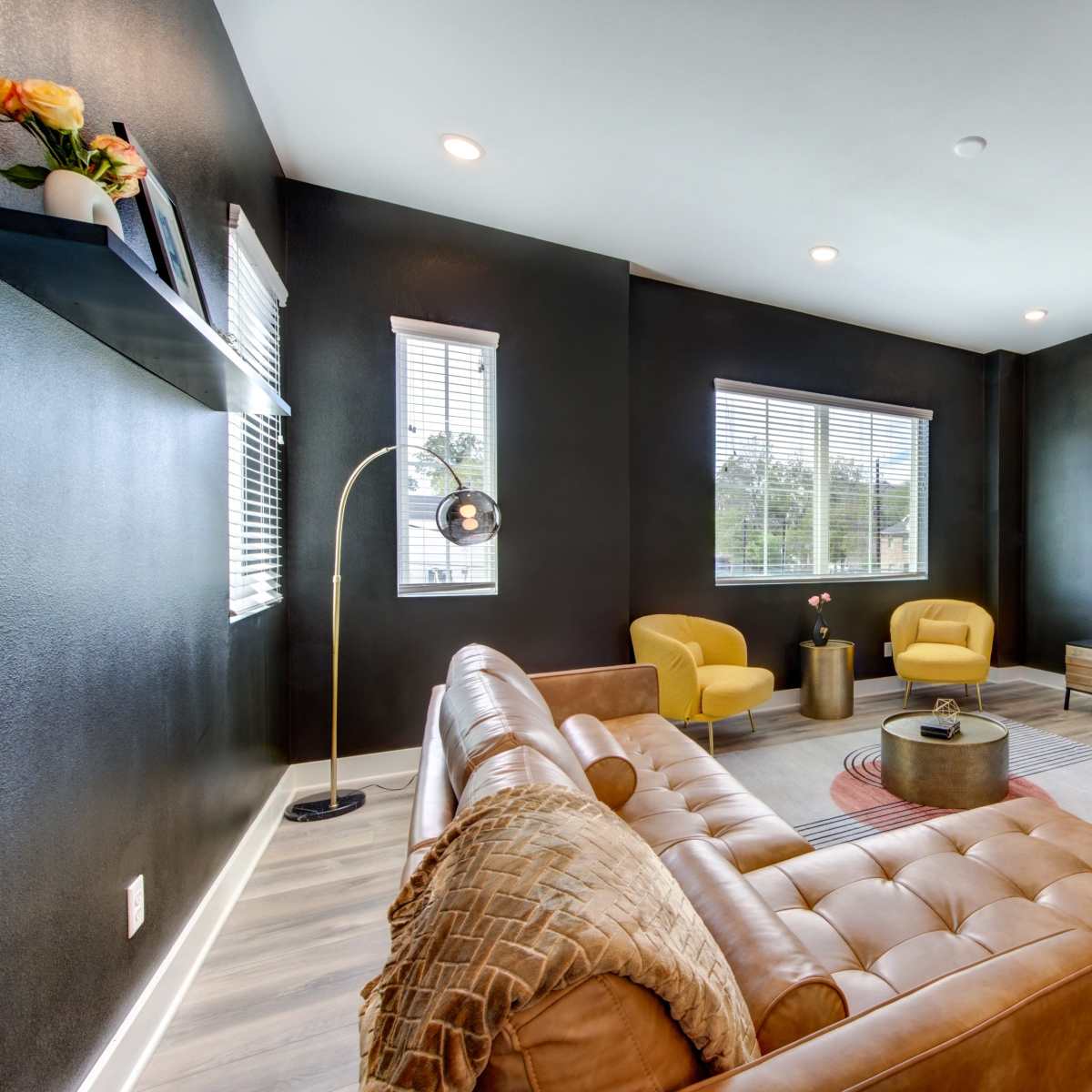 A modern living room featuring a brown leather sofa, two yellow armchairs, a round coffee table, and a wall-mounted television.