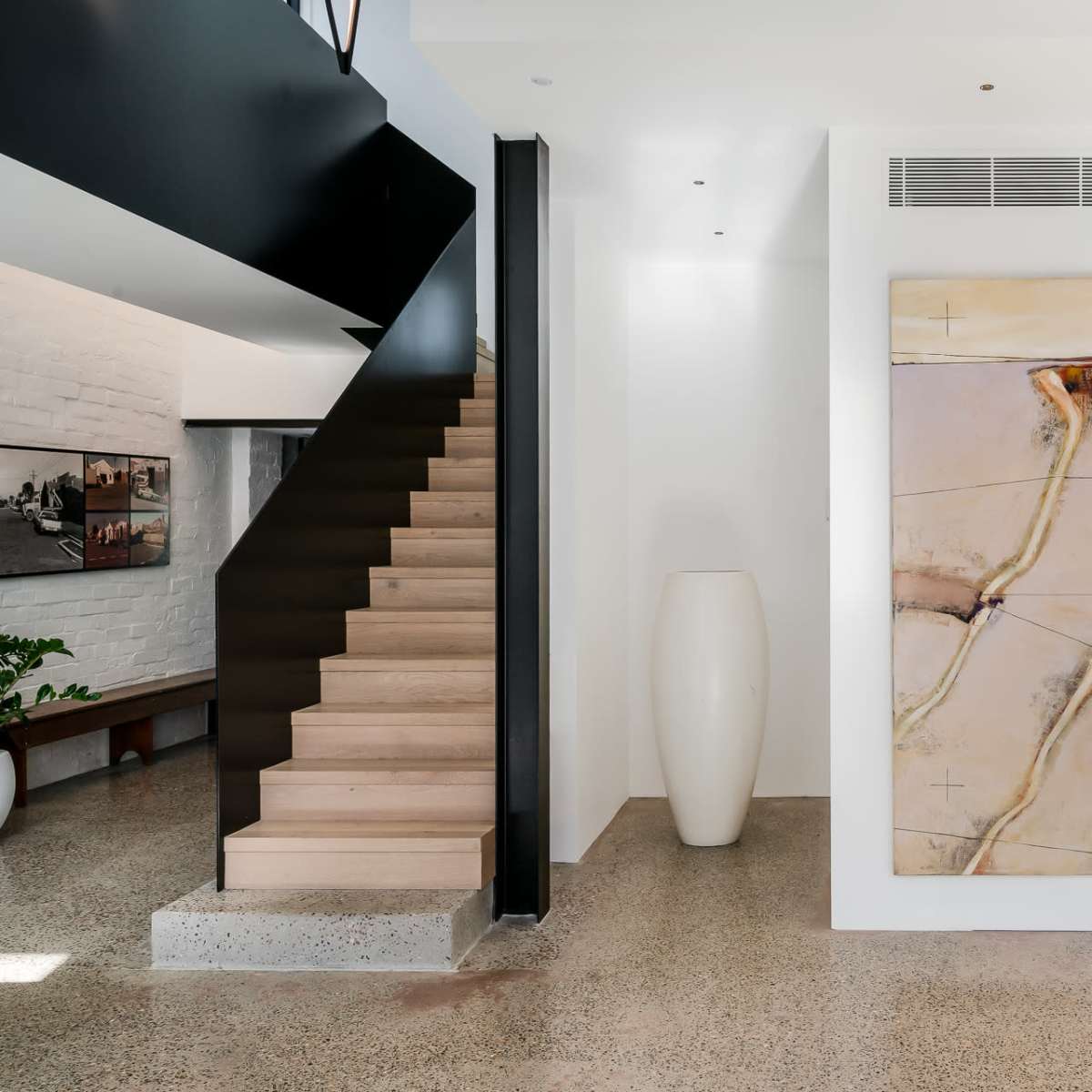 A modern interior with a staircase, a large artwork on the wall, and a minimalistic vase positioned near the stairs.