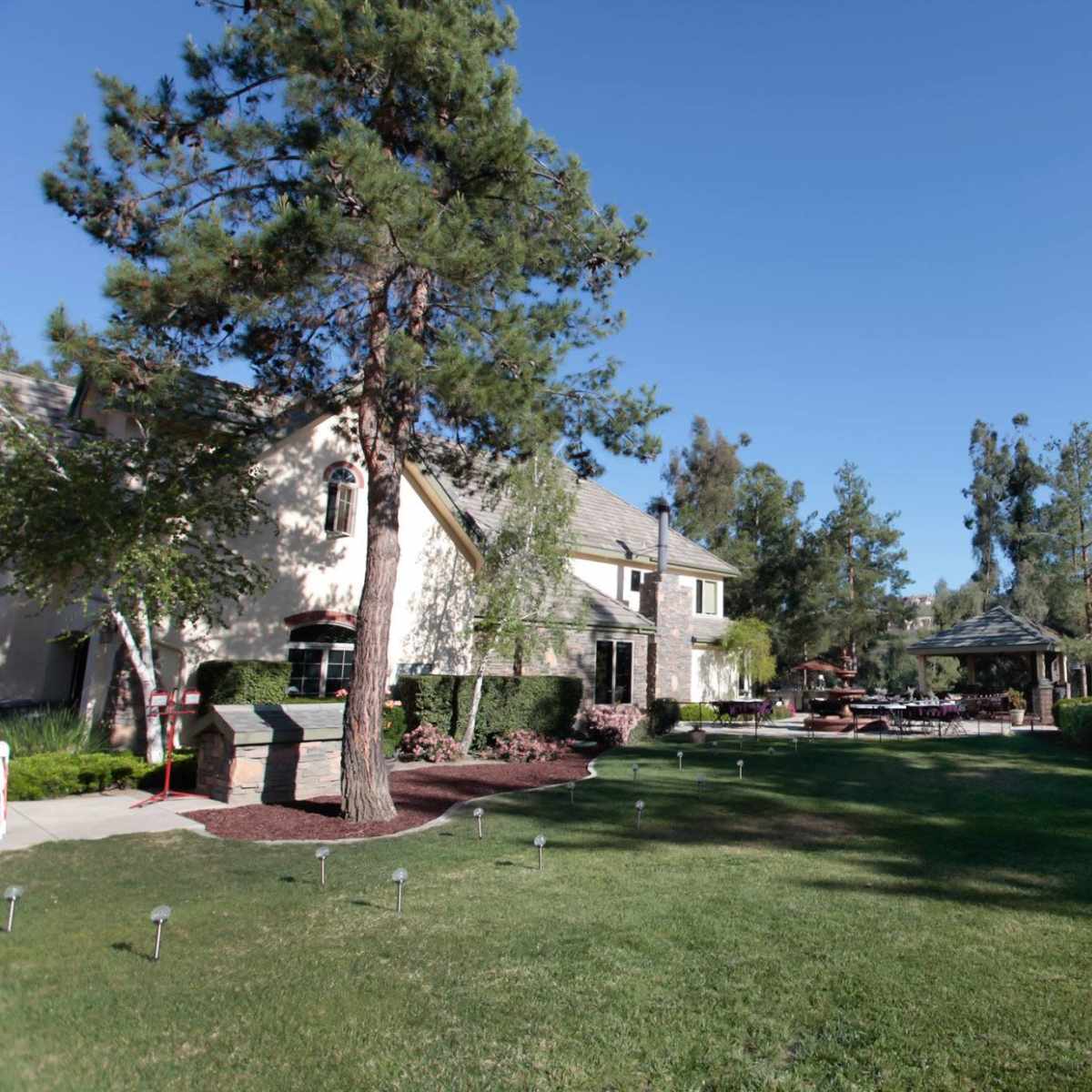 A spacious backyard features a two-story house, a gazebo, and well-maintained landscaping under clear blue skies.