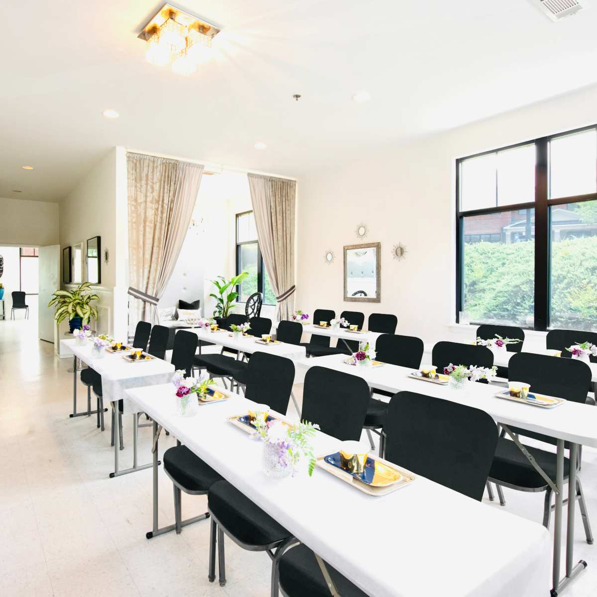 A set up for a dining event with rows of tables adorned with plates and floral centerpieces in a bright, modern room.