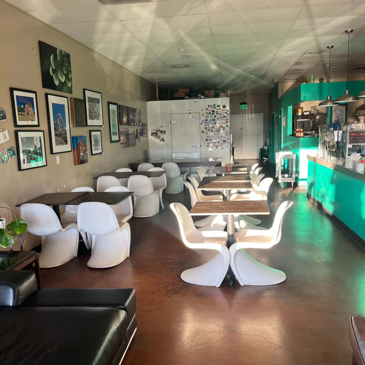 A spacious cafe with white chairs and tables, green accent walls, and various artwork displayed on the walls.
