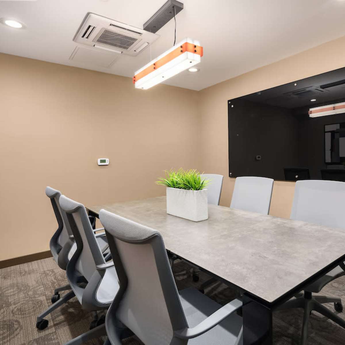 A modern conference room with a rectangular table surrounded by six gray chairs and a wall-mounted black board.