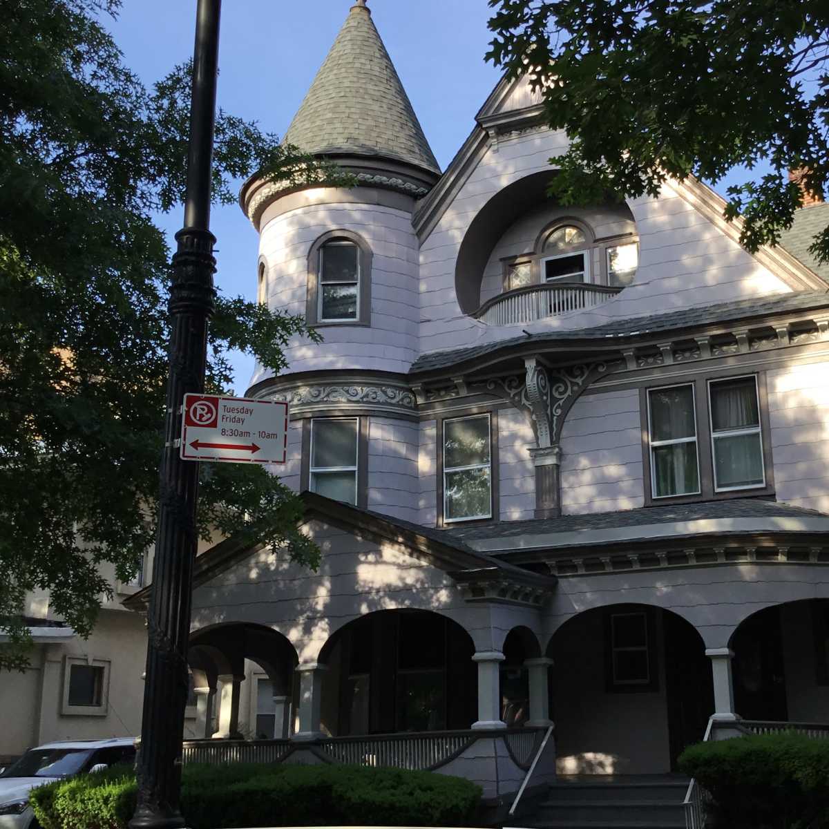A large, Victorian-style house with a pointed turret and wraparound porch is surrounded by trees.