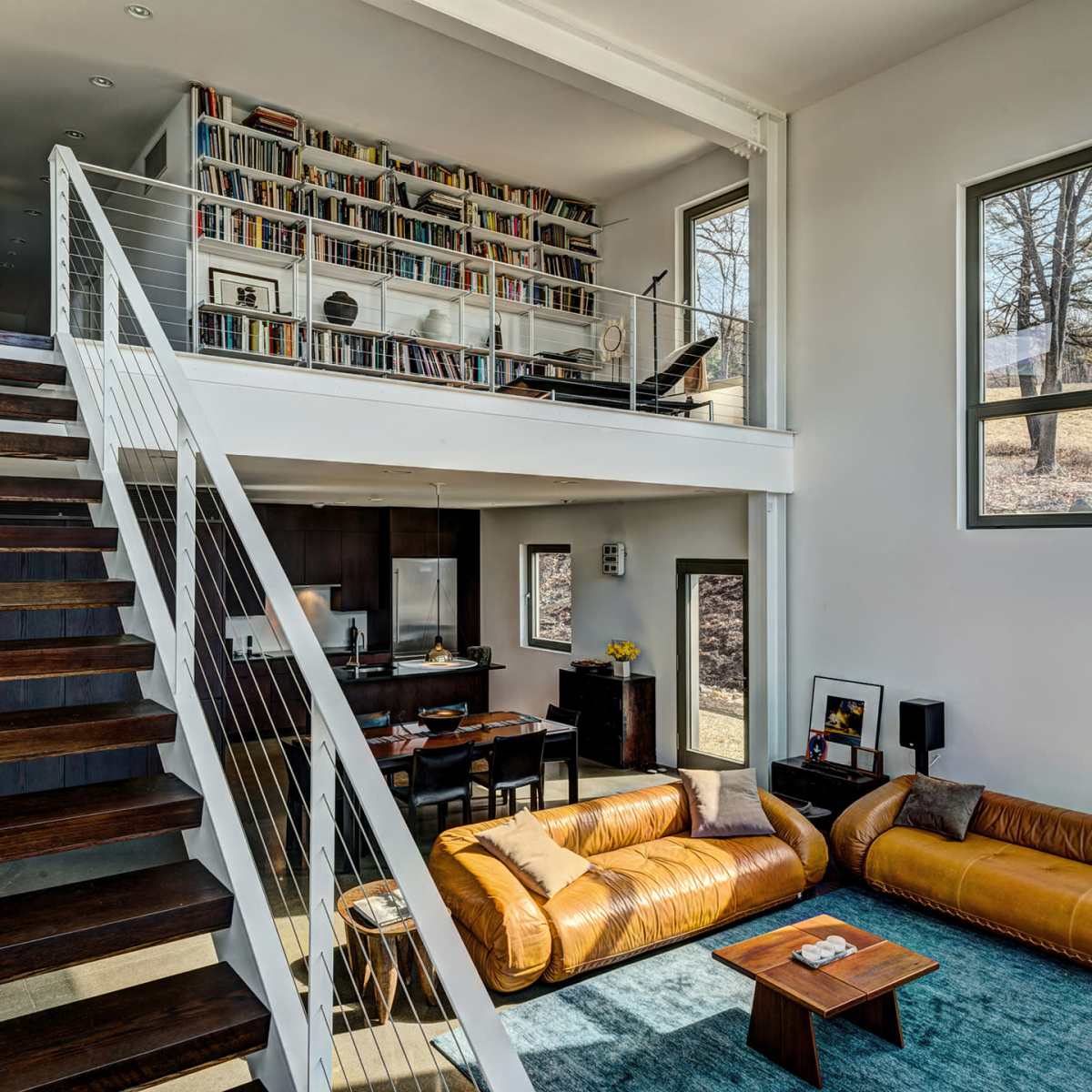 A spacious interior with a two-level living area, featuring a staircase, bookshelves, and a seating arrangement with a coffee table on the ground floor.