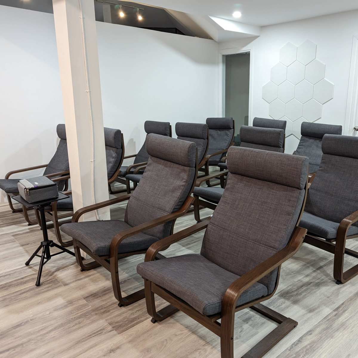 A row of grey reclining chairs arranged in a well-lit room with a white wall and hexagonal paneling.