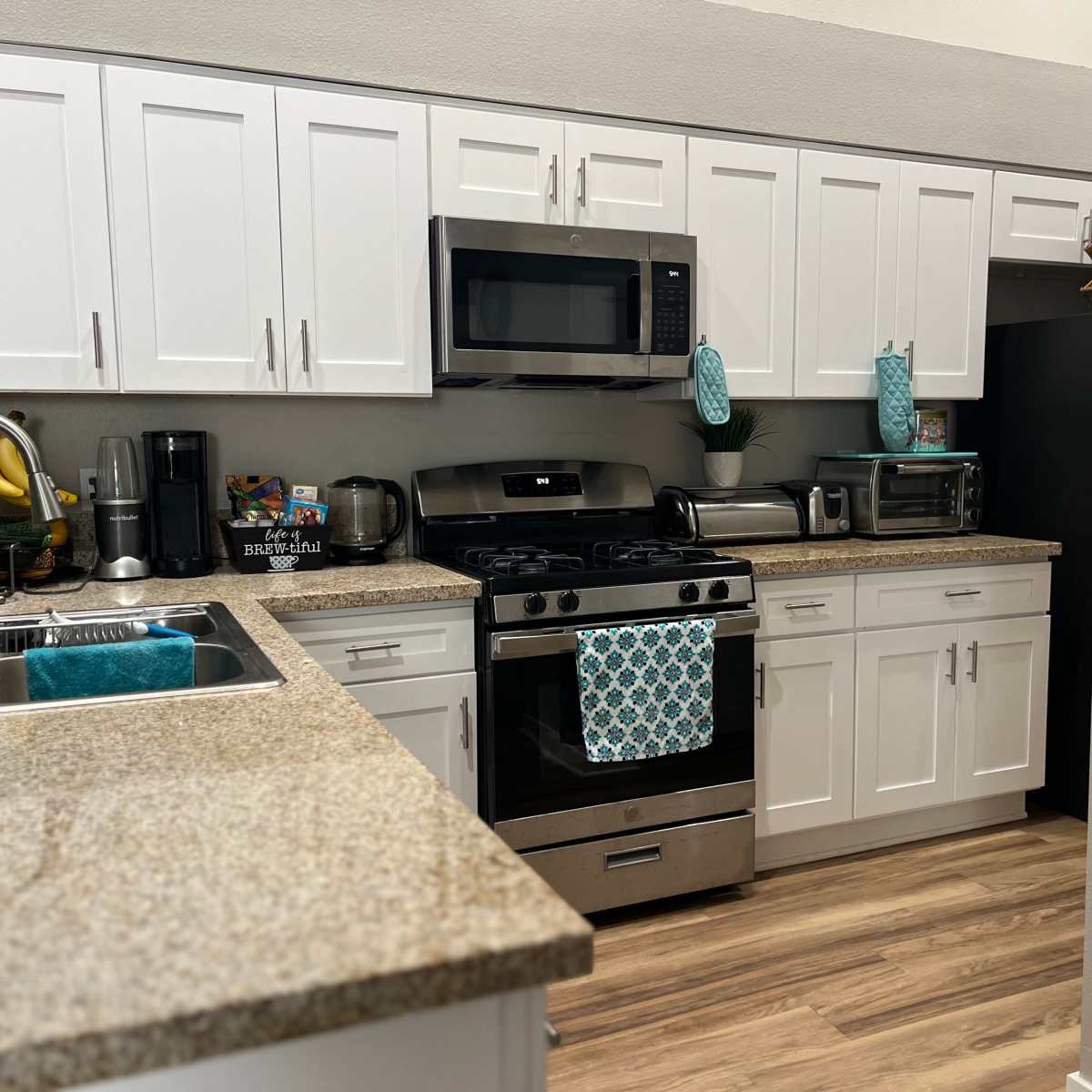 A modern kitchen with white cabinets, a granite countertop, stainless steel appliances, and a blue decorative towel hanging on the oven.