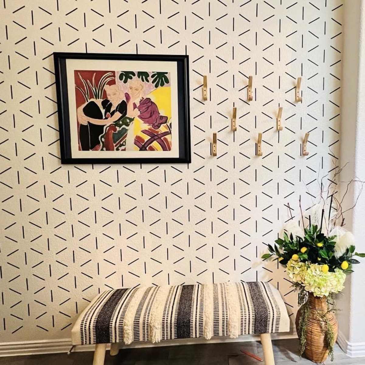 A patterned wall with framed artwork, a decorative bench, a floral arrangement, and framed pictures hanging nearby.