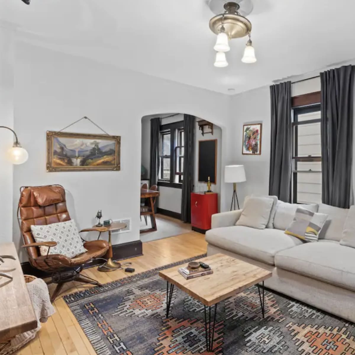 A cozy living room with a light-colored sofa, a wooden coffee table, an armchair, and artwork on the walls.