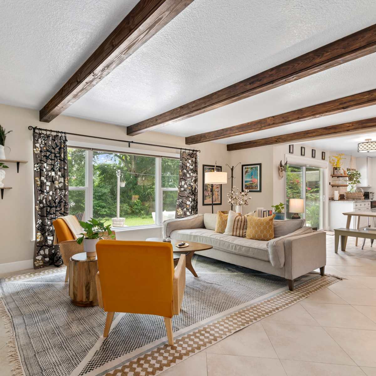 A modern living room features a gray sofa, yellow accent chairs, and large windows overlooking a garden, with wooden beams on the ceiling.