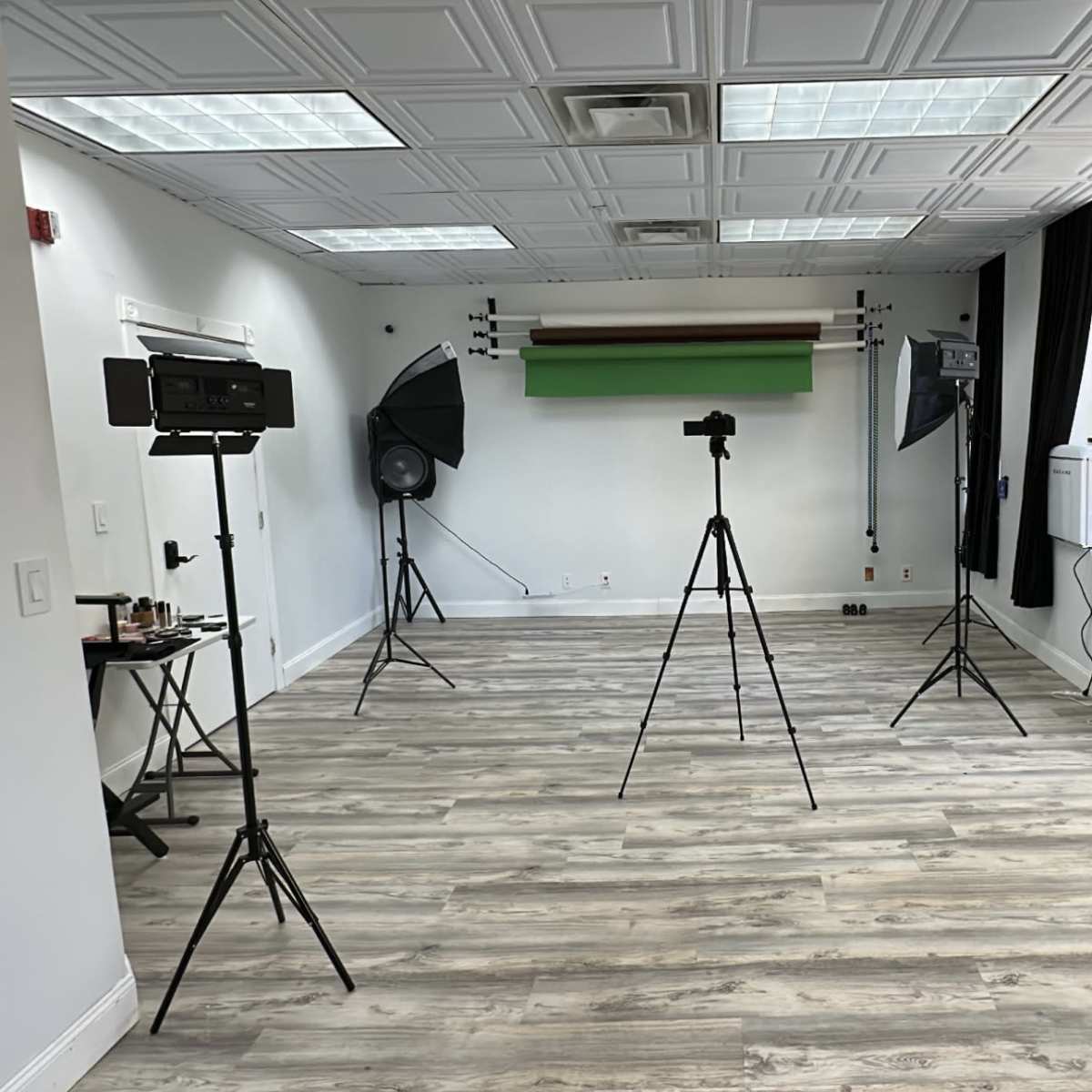 A photography studio with tripods, lighting equipment, and a green backdrop set up in a spacious room.