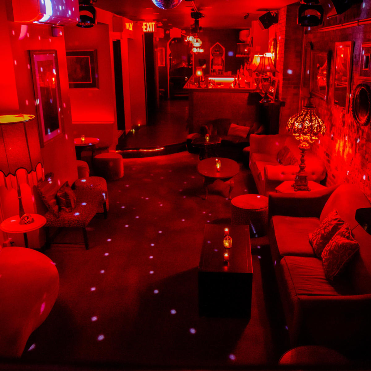 A dimly lit lounge decorated with red lighting, vintage furniture, and disco ball effects on the walls and floor.