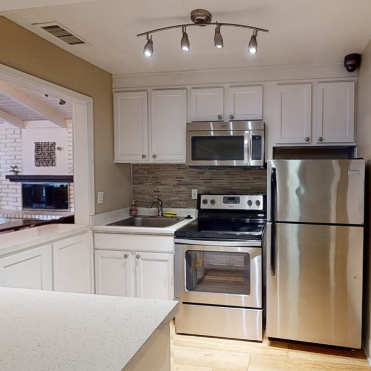 A compact kitchen featuring stainless steel appliances, white cabinetry, and a light-colored countertop.