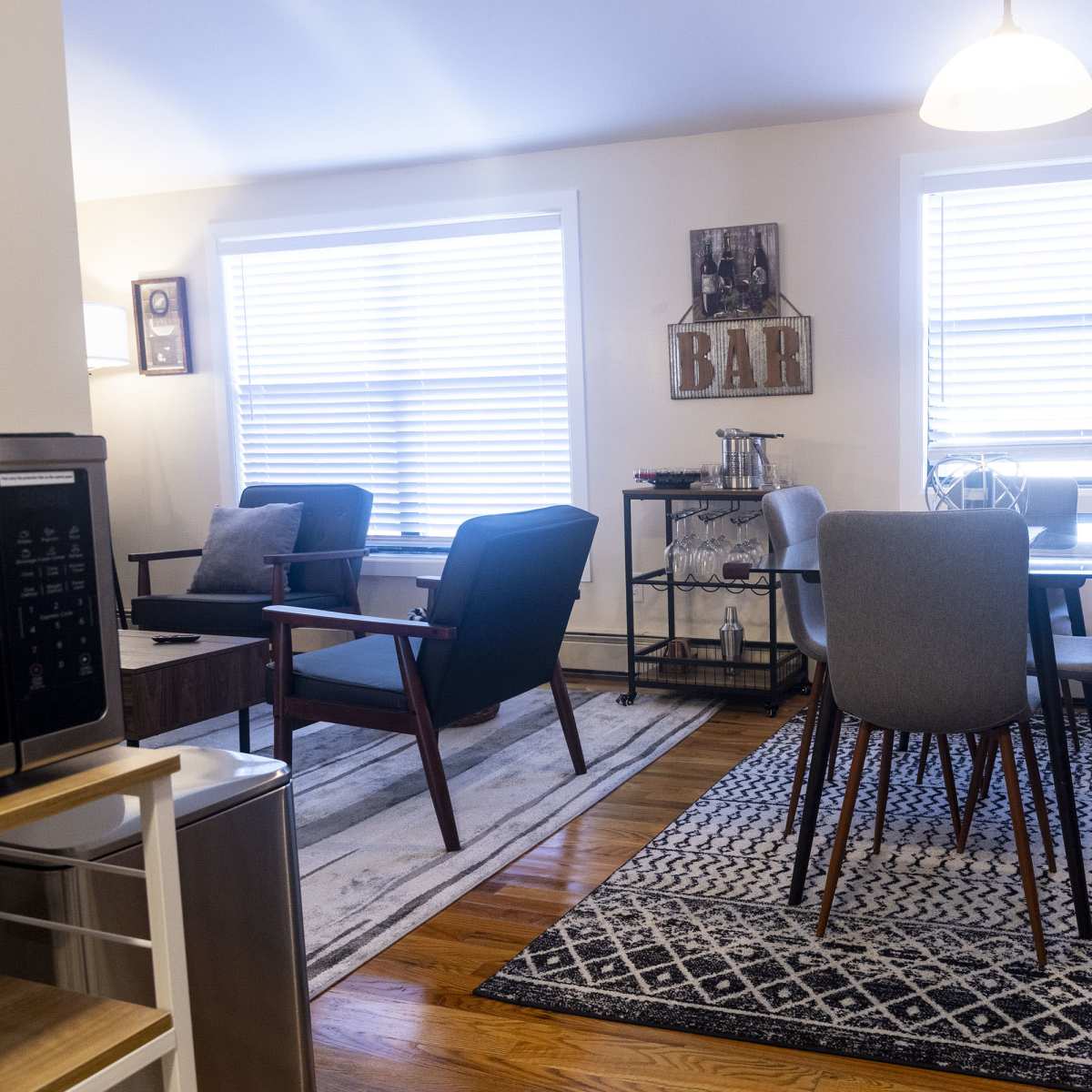 A modern living space featuring a seating area with two armchairs, a dining table with four chairs, and various decorative elements, all illuminated by natural light from two windows.