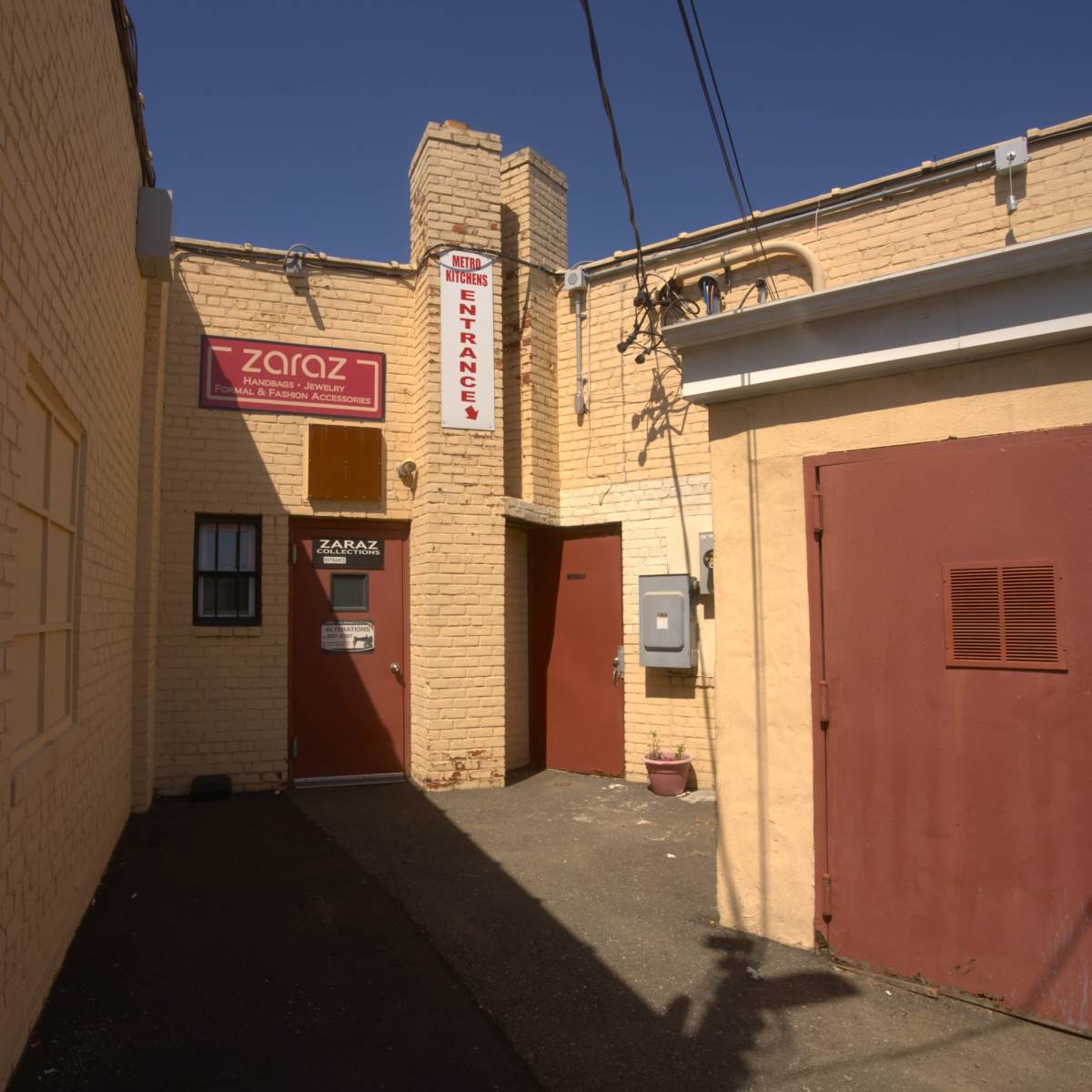 A narrow alleyway with a sign indicating the entrance to a business named "Zaraz," flanked by two buildings and utility meters.