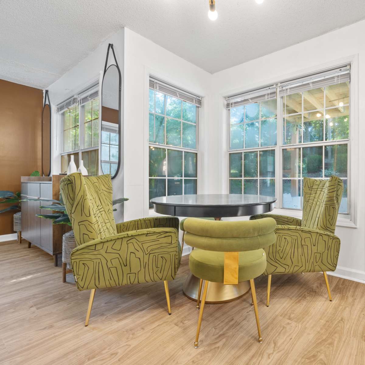 A small dining area features a round black table surrounded by two green chairs and a door leading to an outdoor space.