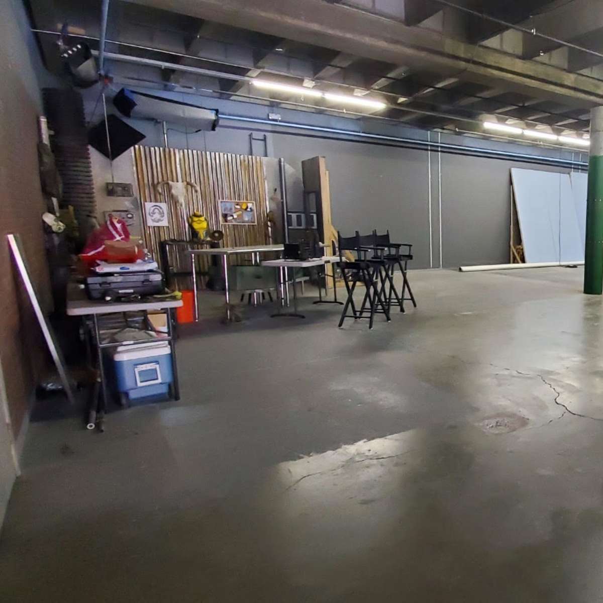 A spacious, empty studio area with concrete flooring, equipped with various props and backdrops along one wall.
