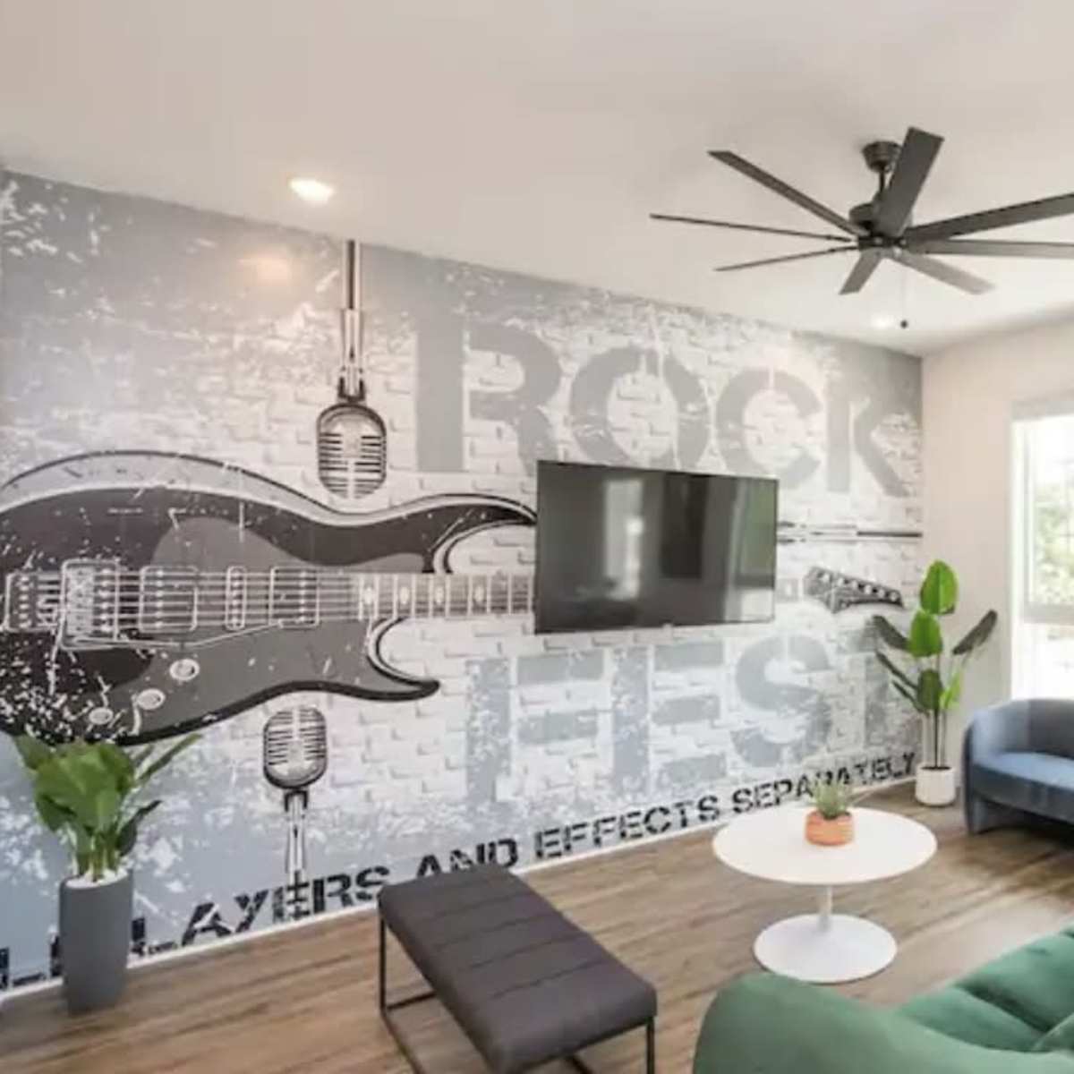 A living room featuring a large guitar mural, a mounted TV, a green couch, and a black coffee table.
