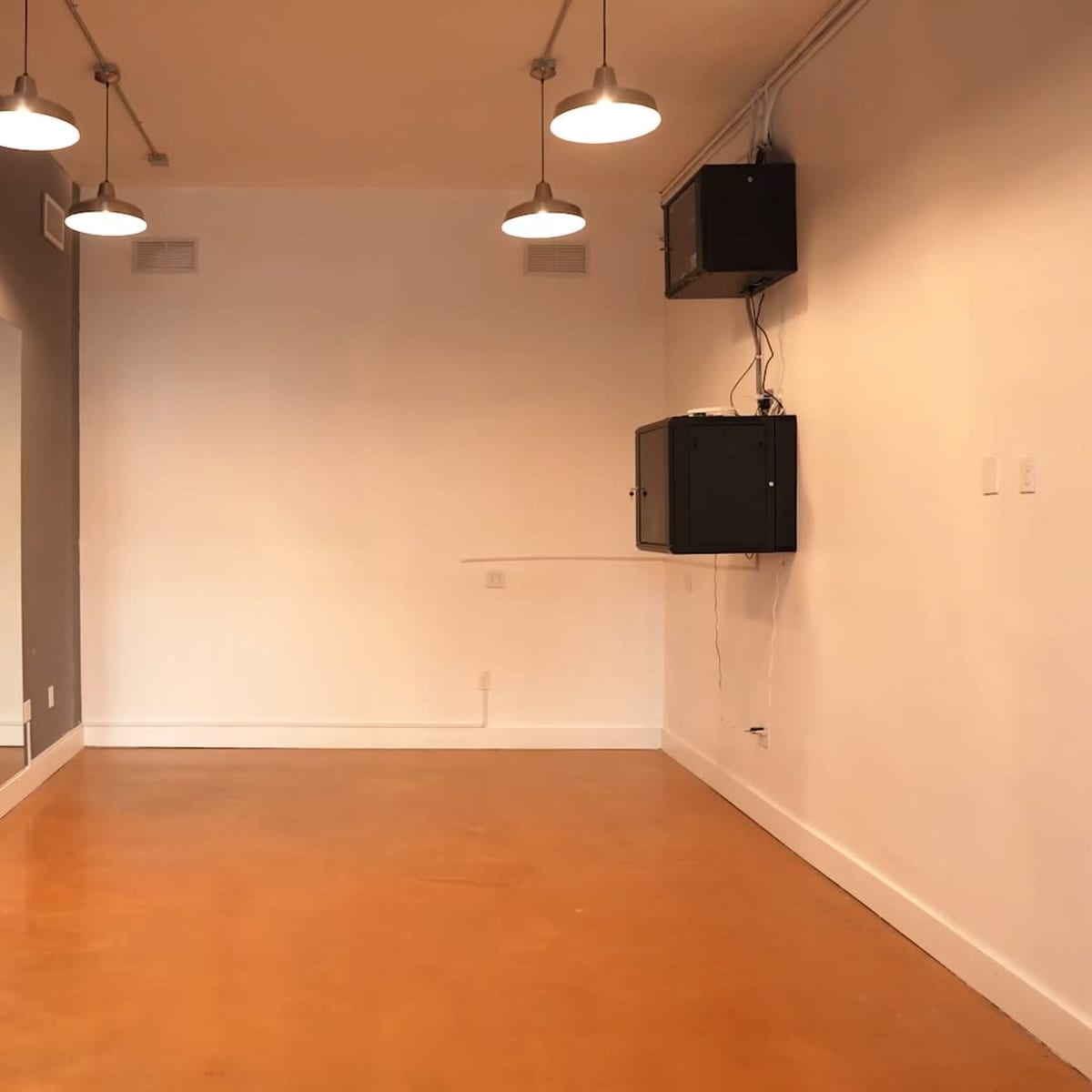 An empty room with a mirror on one wall, concrete flooring, and overhead lights.
