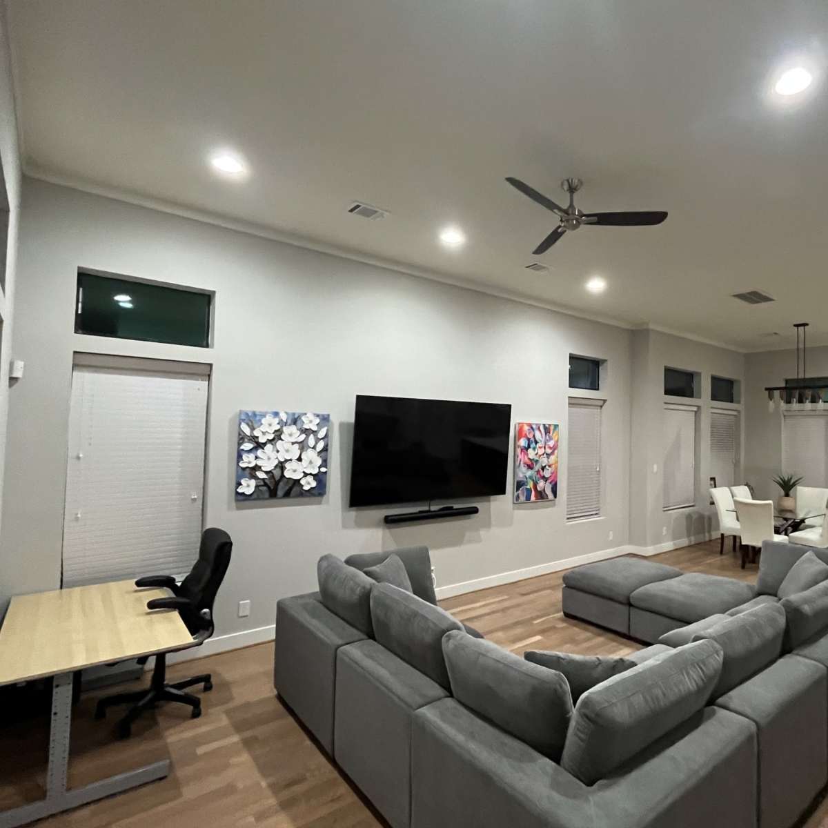 A modern living room with a sectional sofa, a wall-mounted television, and a dining area in the background.