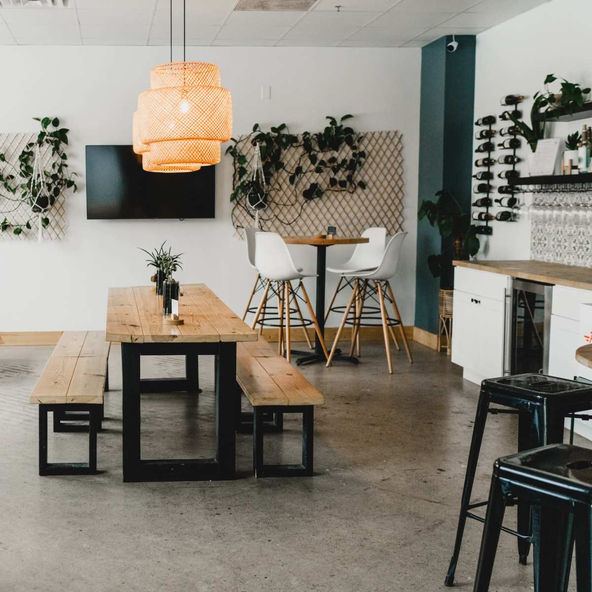 A modern café interior with wooden tables, a large pendant light, and greenery on the walls.