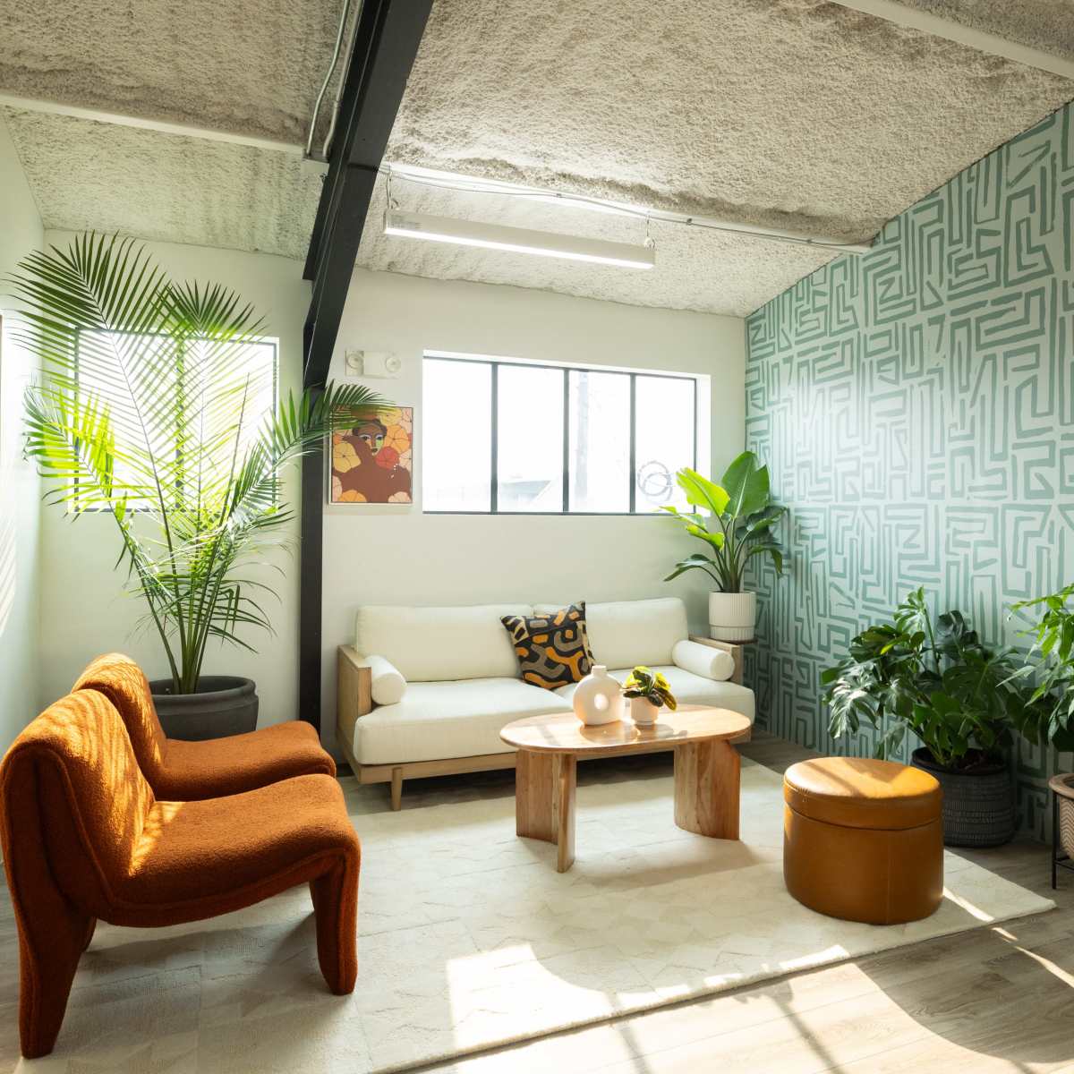A modern living room with a patterned accent wall, a beige sofa, a wooden coffee table, and various indoor plants.