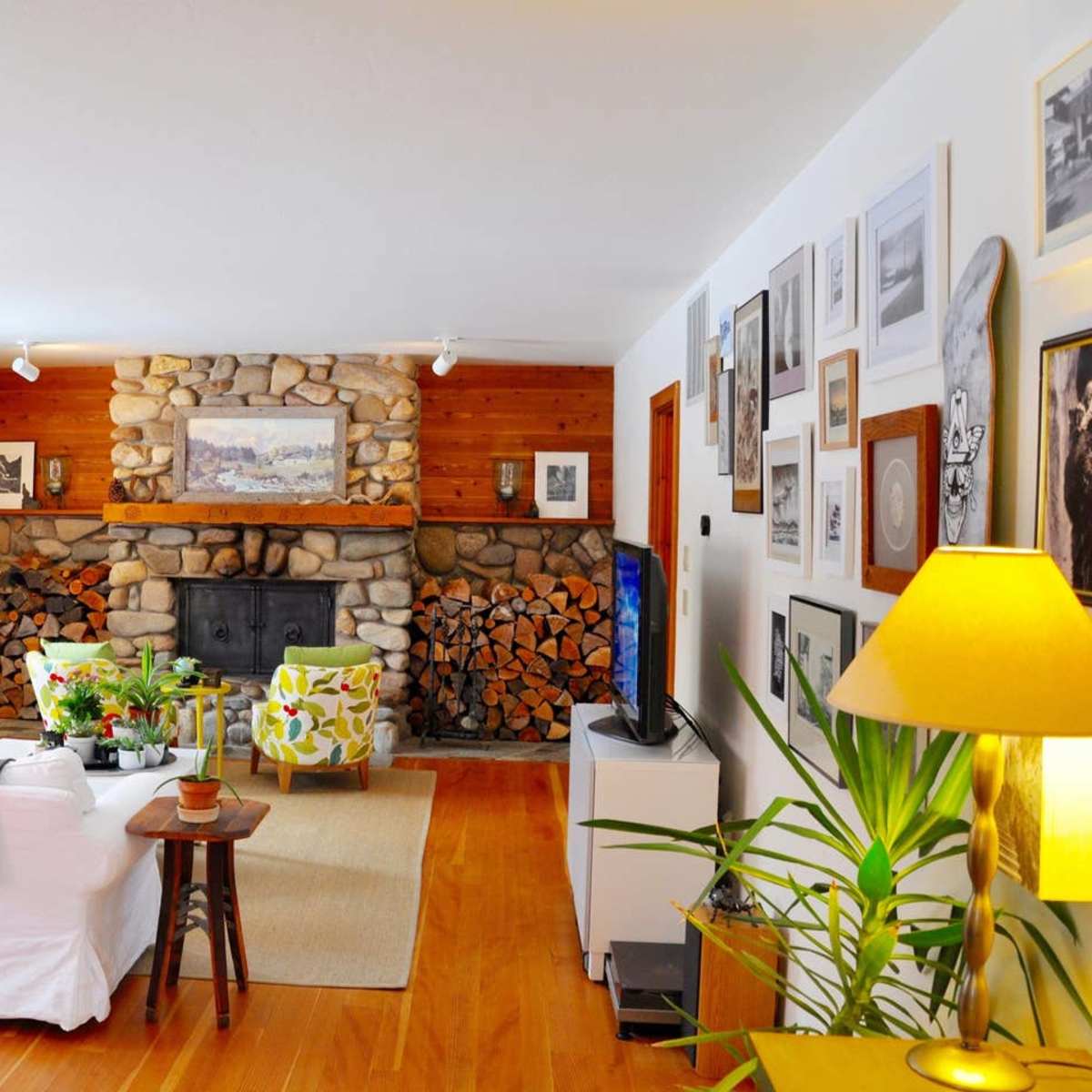 A cozy living room features a stone fireplace, a white sofa, wooden accents, and a wall adorned with framed photographs.