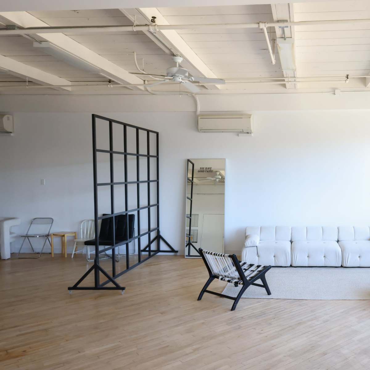 A minimalist, well-lit room with a white sofa, an orange chair, a mirror, and large windows.