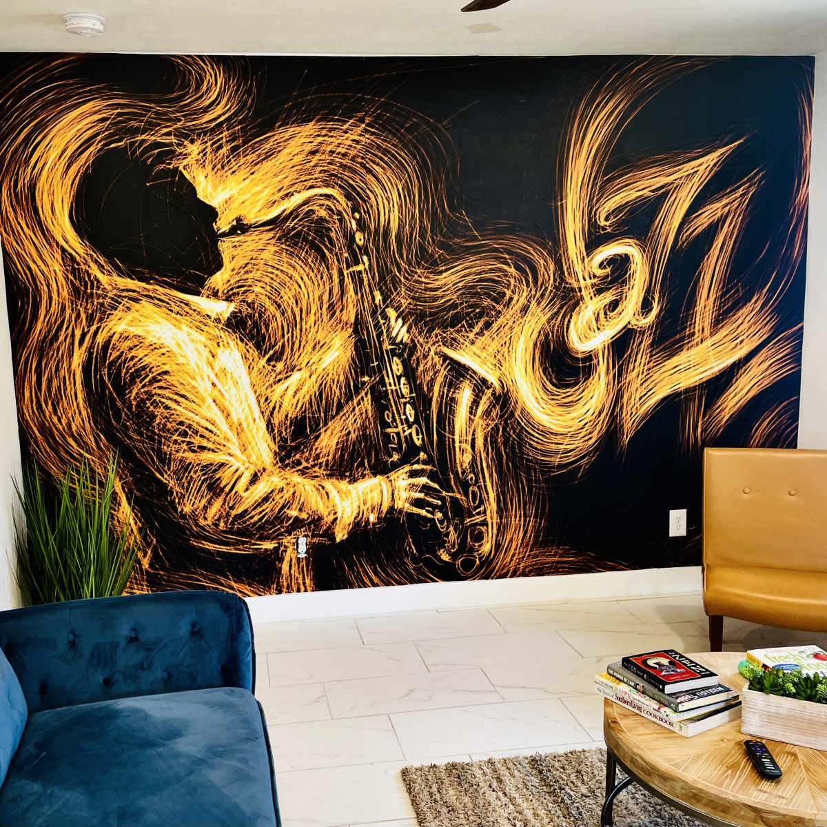 A living room with a wall mural of a saxophonist surrounded by swirling golden lines, alongside a blue couch and a brown armchair.