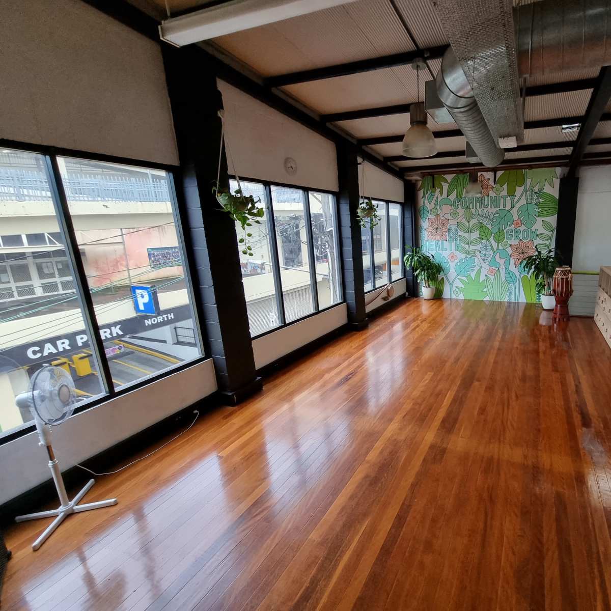 A spacious, brightly lit room with wooden floors, large windows, and a decorative wall featuring greenery.
