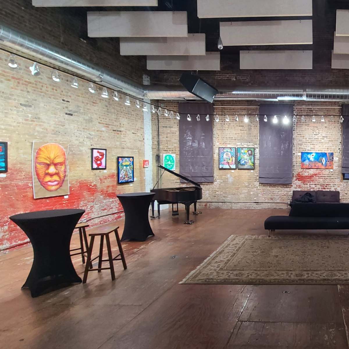 An art gallery featuring colorful paintings on the brick walls, with a piano and several lounge areas arranged around a central rug.